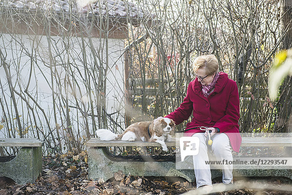 Alte Frau und ihr Hund sitzen draußen auf einer Bank