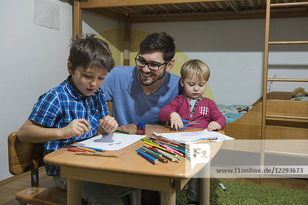 Brüder genießen es  mit Buntstiften zu zeichnen  während der Vater lächelt  München  Deutschland