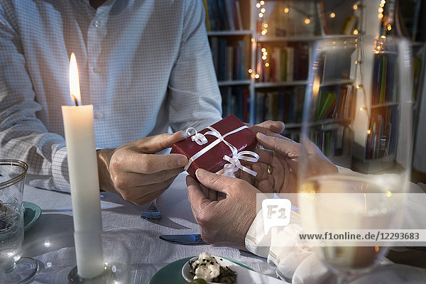 Romantic couple exchanging gift at candlelight dinner