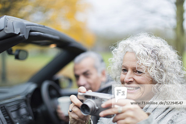 Smiling senior couple using digital camera in convertible