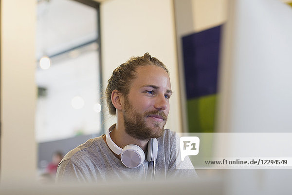 Confident creative businessman with headphones working at computer
