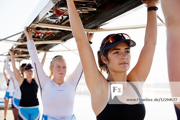 Confident  determined female rowing team lifting scull overhead