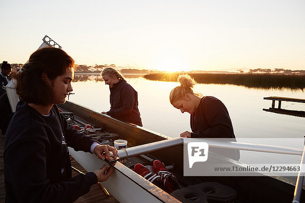Female rowers preparing scull at sunrise lakeside