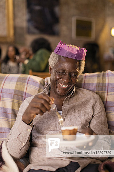 Lächelnder älterer Mann in Weihnachtspapierkrone beim Dessertessen