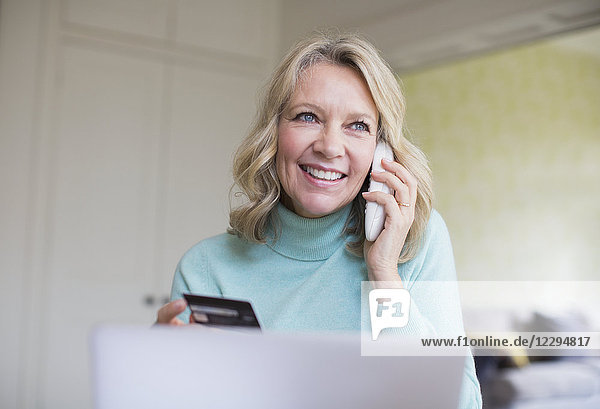 Smiling mature woman with credit card talking on telephone at laptop