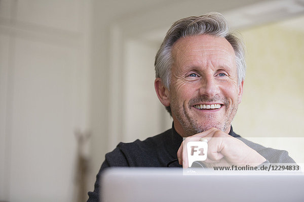 Lächelnder  selbstbewusster männlicher Freiberufler bei der Arbeit am Laptop