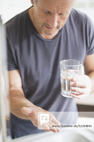 Älterer Mann nimmt Vitamine mit einem Glas Wasser ein