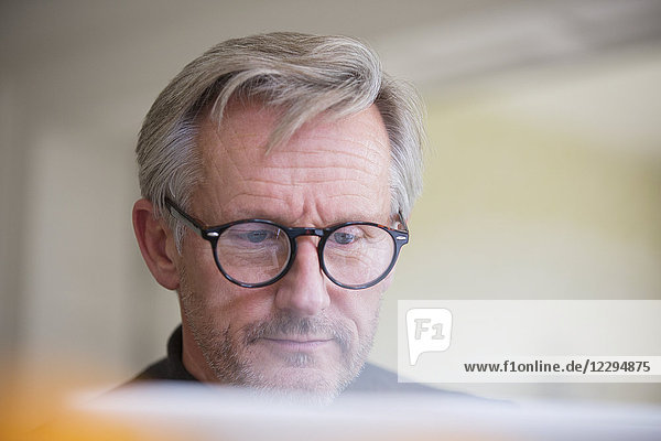 Fokussierter reifer Mann mit Brille arbeitet am Laptop
