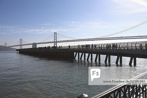 Menschen am Pier mit Oakland Bay Bridge über der Bucht im Hintergrund  San Francisco  USA