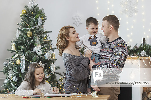 Vater und Mutter halten Sohn um Tochter am Tisch am Weihnachtsbaum sitzend