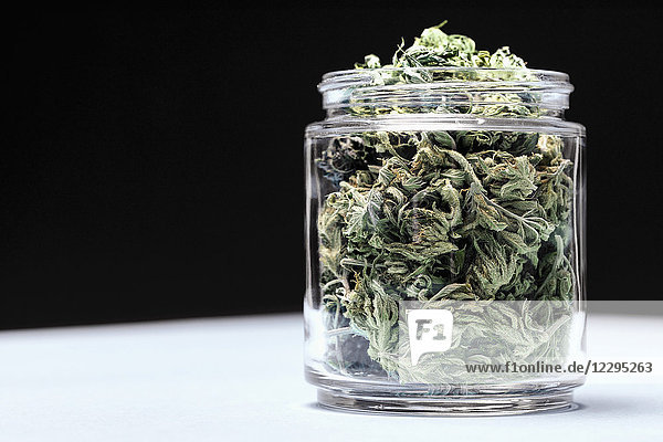 Marihuana-Blätter im Glas auf Tisch vor schwarzem Hintergrund