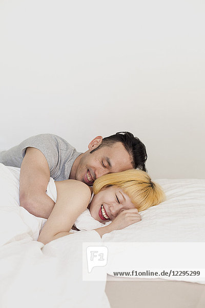 Smiling loving couple sleeping on bed against wall at home