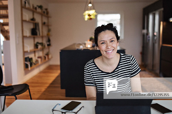 Portrait of smiling mid adult woman using laptop at table in living room