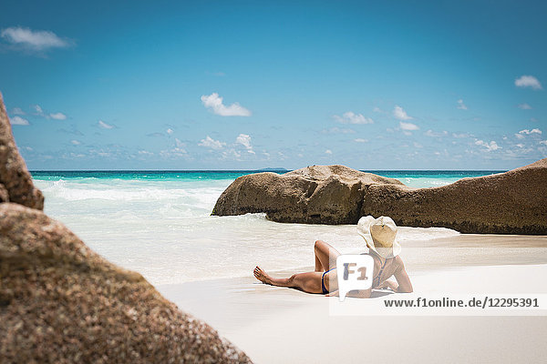 Mittlere erwachsene Frau im Bikini entspannend am Strand gegen den blauen Himmel während des sonnigen Tages  Seychellen