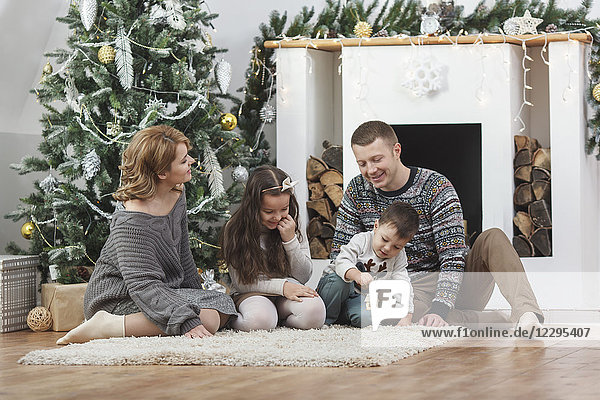 Happy family sitting on rug by Christmas tree at home