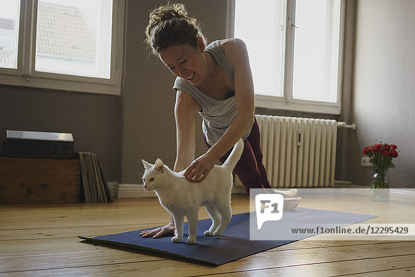 Lächelnde Frau streichelt weiße Katze  während sie zu Hause Yoga übt.