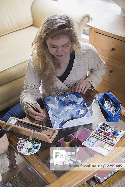 High angle view of young woman making painting while sitting in living room