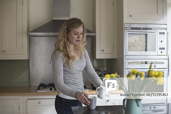 Young woman preparing coffee while standing in kitchen
