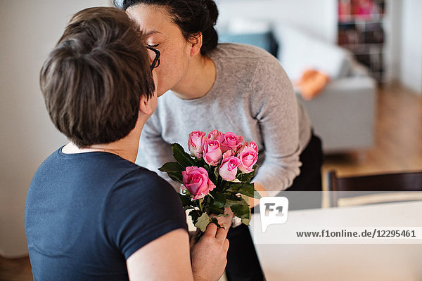 Close-up of lesbian couple kissing while holding pink roses at home