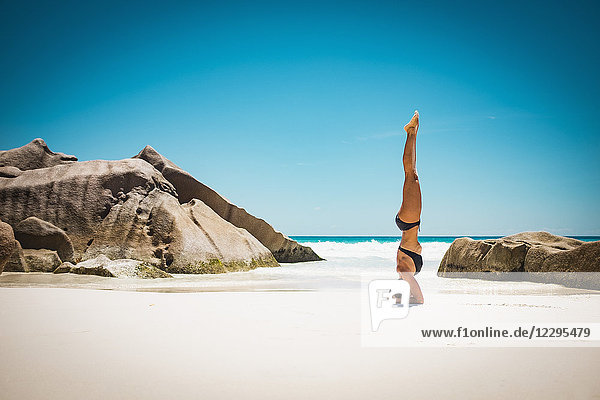 Seitenansicht der mittleren erwachsenen Frau im Bikini beim Kopfstand am Strand gegen den klaren blauen Himmel  Seychellen