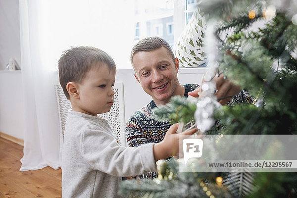 Glücklicher Vater und Sohn schmücken Weihnachtsbaum zu Hause