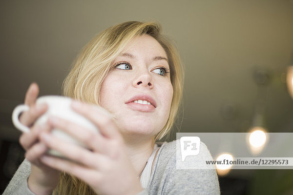 Nachdenkliche junge Frau mit Kaffeetasse zu Hause