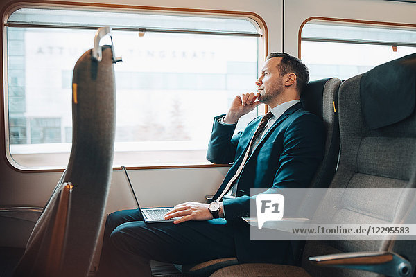 Thoughtful businessman with laptop traveling in train