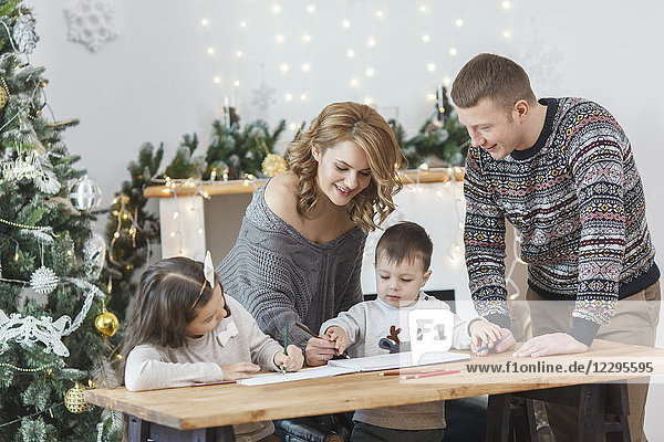 Mann betrachtet Frau und Kinder beim Zeichnen im Buch auf dem Tisch zu Hause
