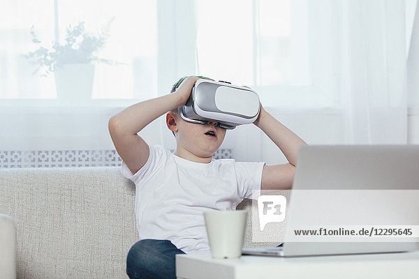 Boy wearing virtual reality headset while sitting on sofa at home