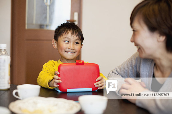 Lächelnder Junge mit Lunchbox und Blick auf die Mutter im Haus