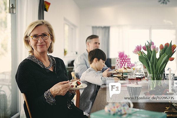 Portrait of smiling grandmother having cake while sitting with family at table during party