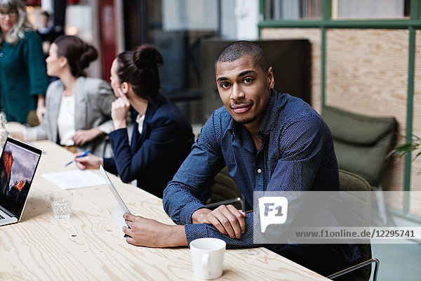 Portrait of young businessman sitting with female colleagues at table in office meeting