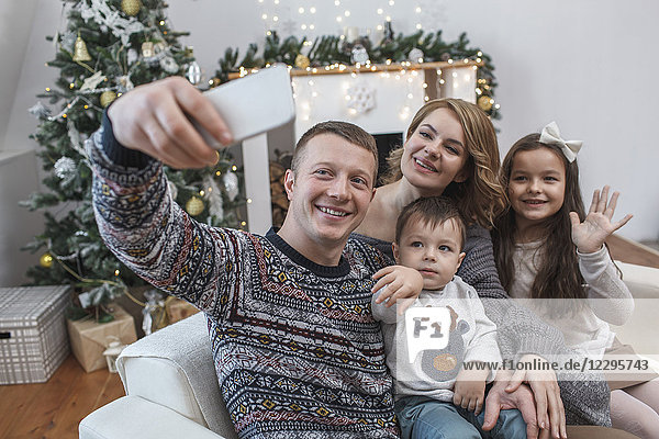 Glücklicher Mann nimmt Selfie mit Familie auf Sofa zu Hause während Weihnachten