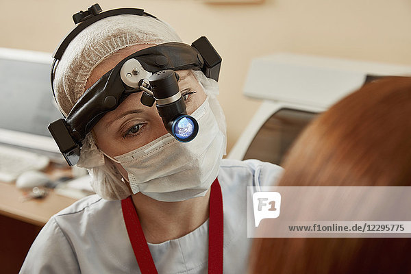 Chirurg mit Stirnlampe bei der Untersuchung einer Patientin im Krankenhaus