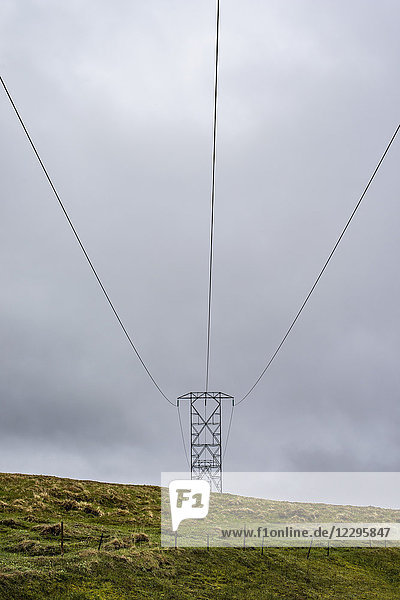 Flachwinkelansicht des Strommastes auf grüner Wiese gegen bewölkten Himmel  Highlands  Island