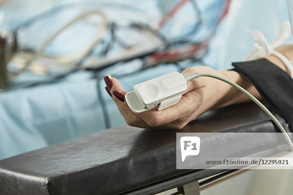 Abgeschnittenes Bild eines Patienten  der ein Pulsoximeter trägt  während er im Krankenhaus auf dem Bett liegt.