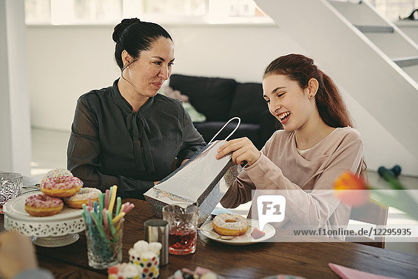 Smiling mother looking at excited daughter with gift during birthday party