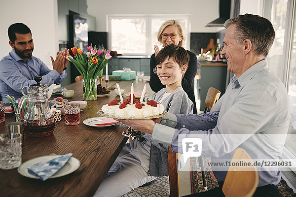 Smiling boy with grandparents and father with birthday cake at table