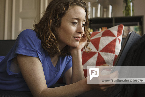 Frau mit digitalem Tablett auf dem Sofa zu Hause