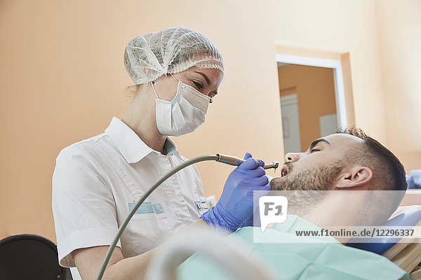 Zahnarzt mit OP-Maske und Kappe bei der Untersuchung des männlichen Patienten