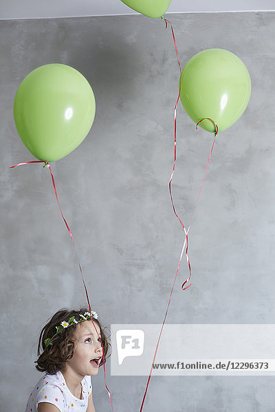 Fröhliches Mädchen hält grüne Luftballons gegen graue Wand