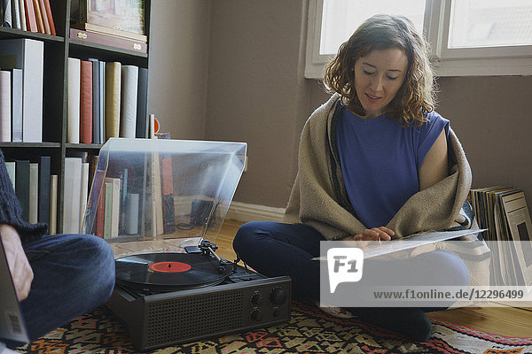 Woman sitting with record by turntable and man on carpet at home