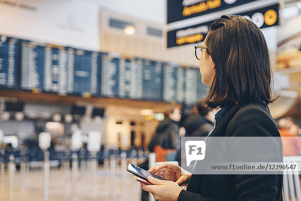 Mid adult businesswoman holding mobile phone while standing in airport