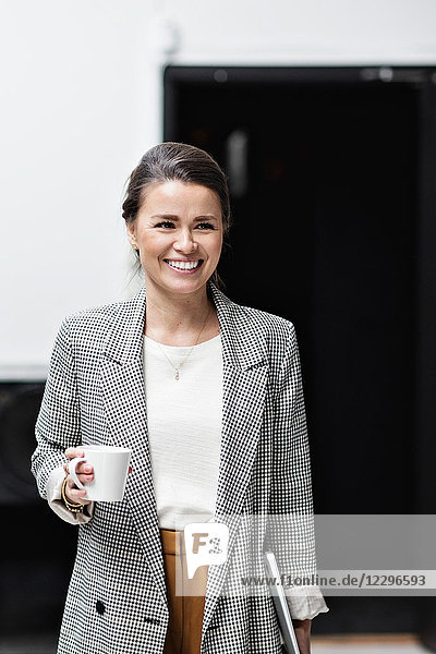 Portrait of smiling businesswoman looking away while holding coffee cup at office