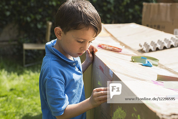Jungenmalerei auf Pappspielhaus im Hinterhof bei Sonnenschein