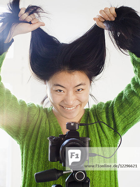 Porträt einer fröhlichen jungen Frau  die im Stehen mit der Kamera Haare hält.
