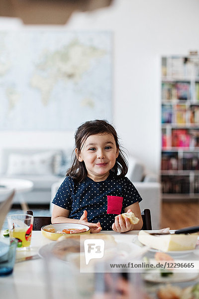 Portrait of cute smiling girl having breakfast at table in house