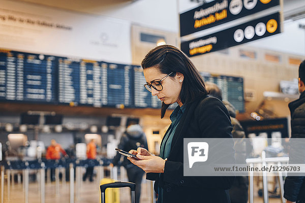 Side view of mid adult businesswoman using mobile phone in airport terminal