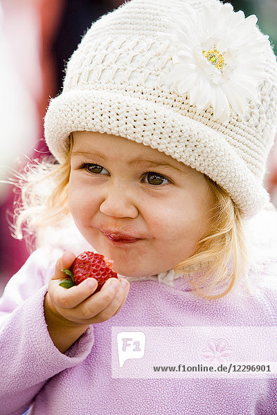 Kleines Mädchen genießt frische Erdbeeren auf dem Bauernmarkt