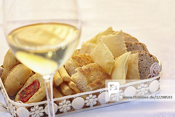 Brot und Gebäck auf einem Tablett vor einem Glas Weißwein